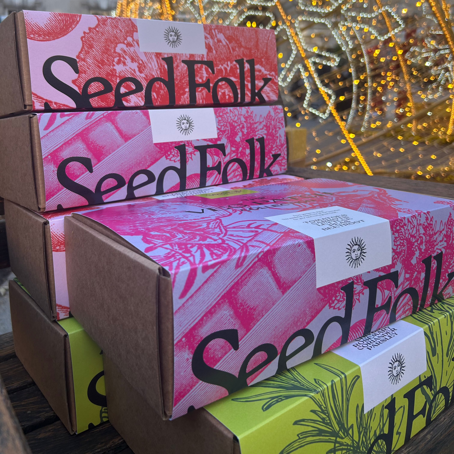 Seed Folk Gift Boxes stacked in front of Christmas lights.